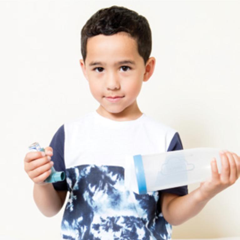 A child holding an inhaler and spacer separately before use.