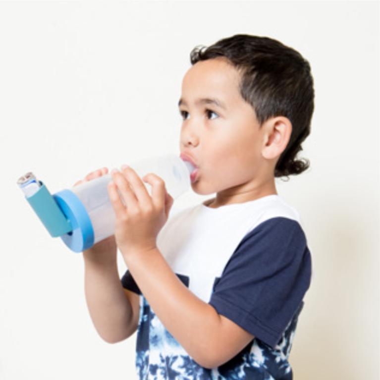 A child breathing in through a spacer while holding the inhaler and spacer in place.