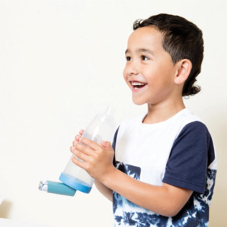 A child holding an inhaler and spacer after use.