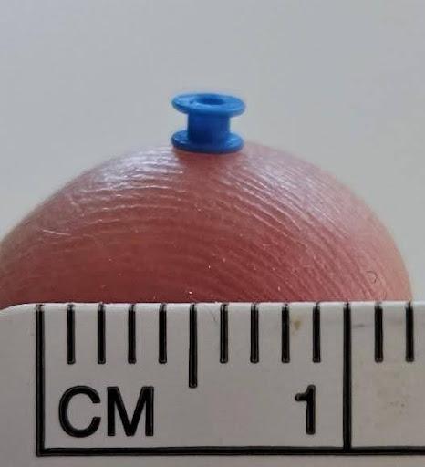 Close up photo of a blue grommet on a finger tip with a ruler to show the size