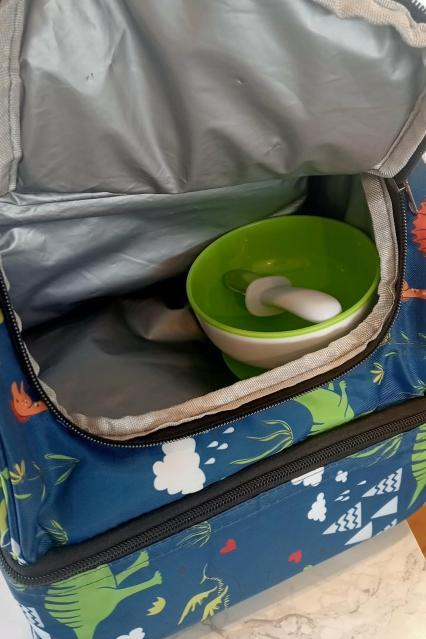 An open insulated cooler bag containing tube feeding supplies, including a bowl and spoon inside.