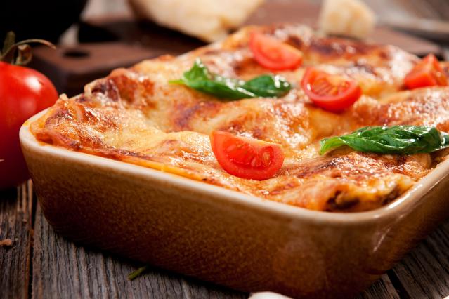 A baked pumpkin and spinach lasagna in a ceramic dish, topped with melted cheese, cherry tomatoes, and basil leaves.