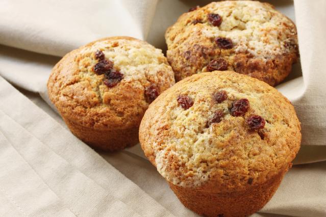 Three golden-brown muffins with raisins on top, sitting on a light-coloured cloth.
