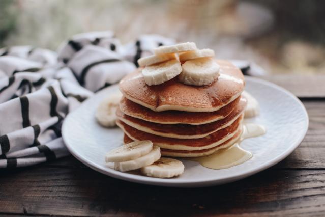 A stack of pancakes topped with sliced banana and syrup on a white plate, with extra banana slices on the side.