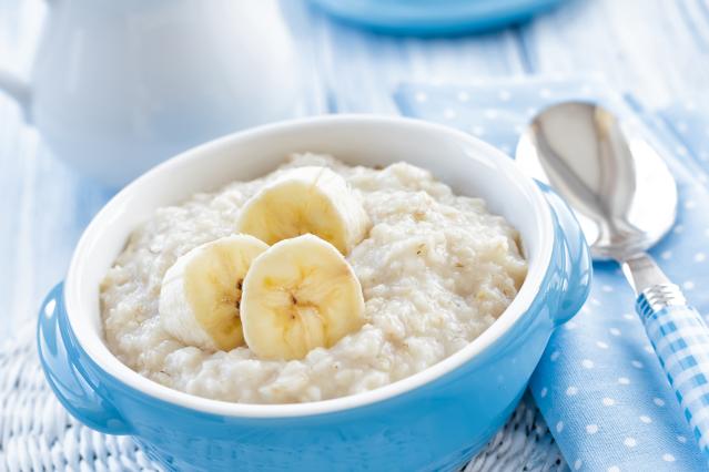 A bowl of creamy porridge topped with sliced banana, beside a spoon on a blue table setting.