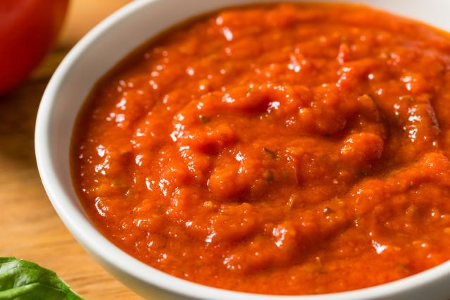 A bowl of thick red tomato sauce on a wooden surface.