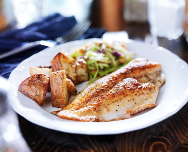 BBQ grilled fish fillet served on a white plate with roasted potatoes and salad.