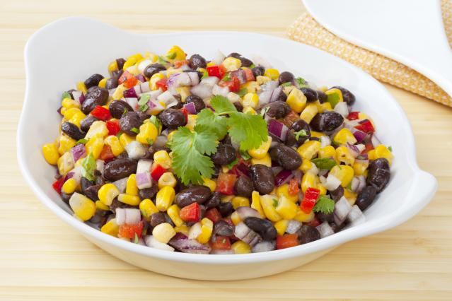 Black bean and corn salad with diced red onion, capsicum and coriander served in a white bowl.