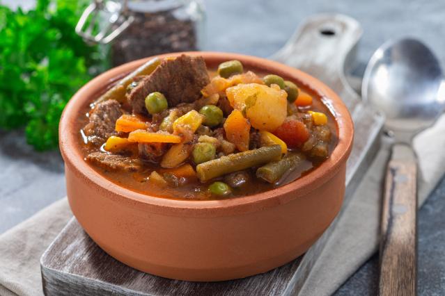 Beef and vegetable stew with peas, beans, potato and carrot served in a brown bowl.