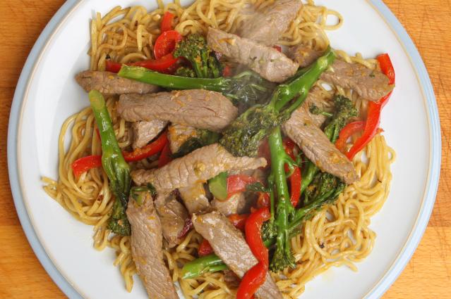 Beef stir-fry with noodles, broccoli and red capsicum served on a white plate.
