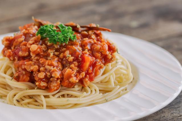 Spaghetti topped with a chunky tomato-based mince and lentil sauce and parsley garnish on a white plate.
