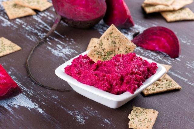 Bright pink beetroot dip served in a small white bowl with crackers on a wooden table.