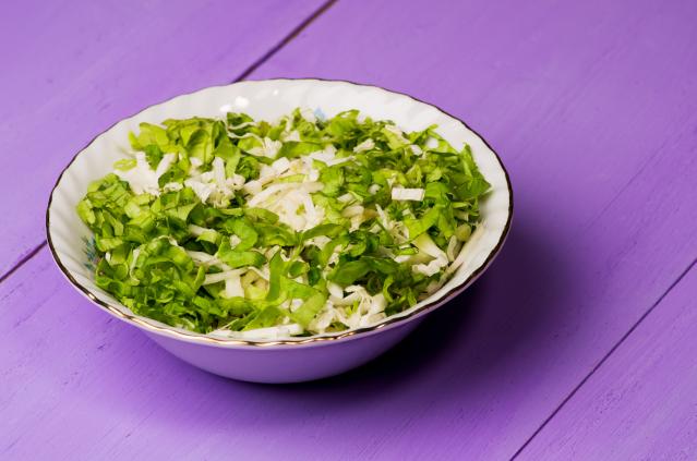 A bowl of shredded green bok choy and cabbage salad on a purple wooden table.