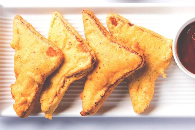 Golden toasted sandwich triangles coated in batter and served with dipping sauce on a white plate.