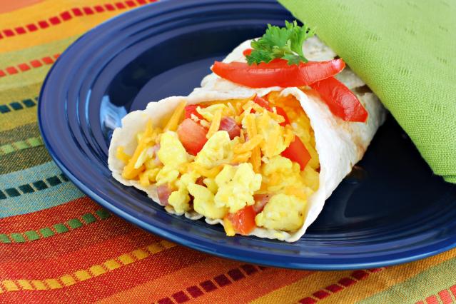 A breakfast burrito filled with scrambled egg, cheese, and red capsicum on a blue plate, garnished with parsley and slices of red capsicum.