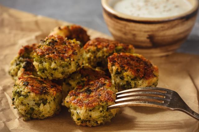 Small golden broccoli patties on baking paper with a fork and dipping sauce in the background.