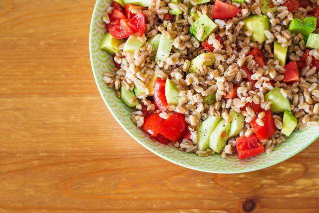Bowl of brown rice salad with avocado, tomato and cucumber on a wooden table.