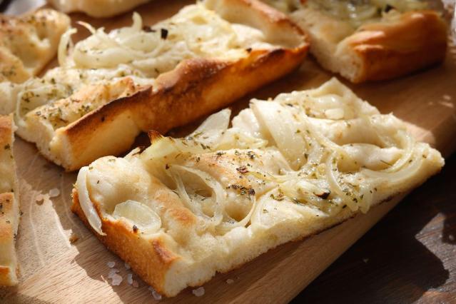 Slices of white pizza topped with onion, potato, feta and herbs on a wooden board.