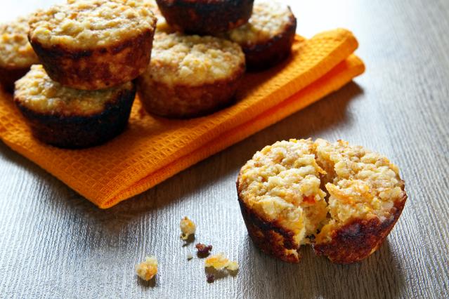 Small carrot and apple muffins on an orange cloth, with one muffin broken open on a wooden table.
