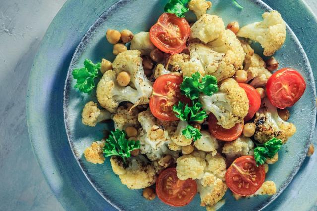 Roasted cauliflower and chickpea salad with cherry tomatoes and parsley served on a grey plate beside a fork and knife.