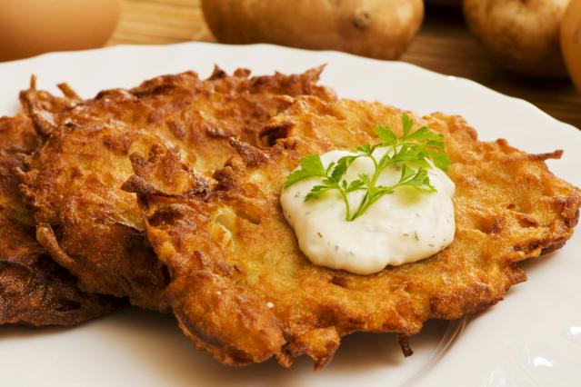 Golden cauliflower fritters on a white plate topped with a dollop of yoghurt sauce and parsley.