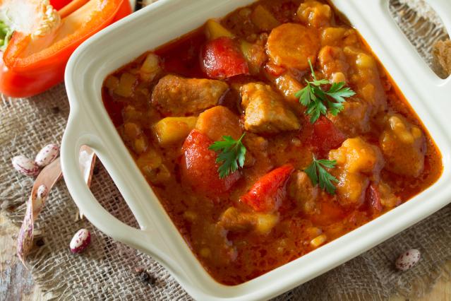 Chicken and vegetable casserole with carrots and capsicum in a tomato-based sauce, served in a white dish.