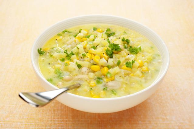 bowl of creamy corn chowder with potato, beans, and parsley, with a spoon resting in the bowl.