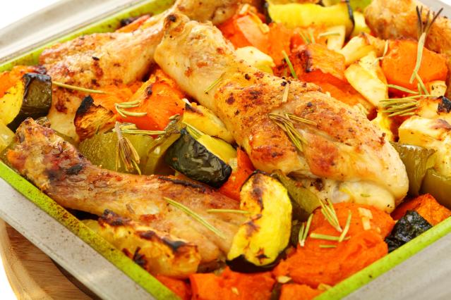 Roasted chicken pieces with pumpkin, zucchini, and other roasted vegetables in a baking dish, garnished with rosemary.