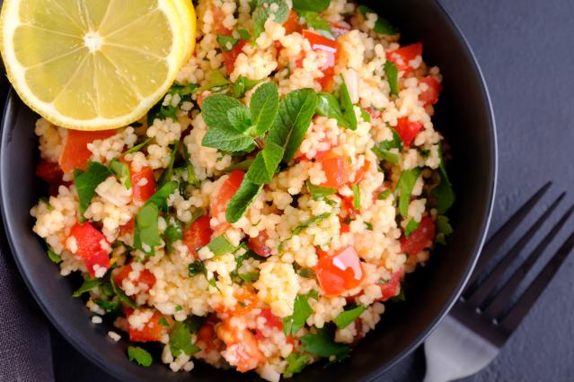 Bowl of couscous salad with chopped tomato, fresh herbs and a slice of lemon.