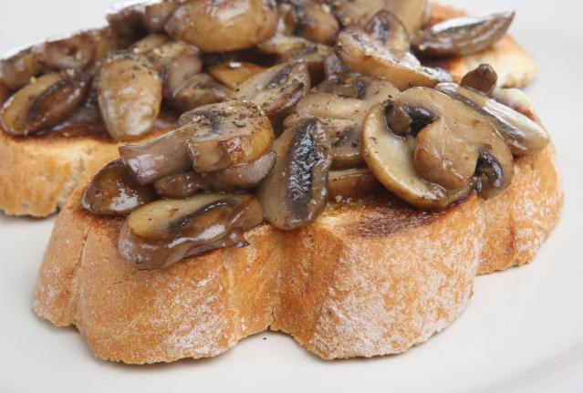 Sautéed mushrooms on toasted bread slices, served on a white plate.