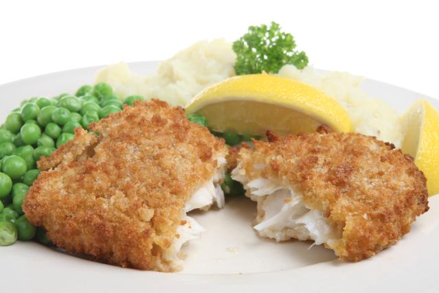 Crumbed fish fillets served with mashed potato, green peas, and lemon wedges on a white plate.