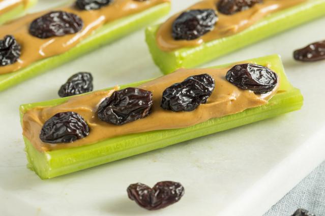 Celery sticks filled with peanut butter and topped with raisins, arranged on a white board.