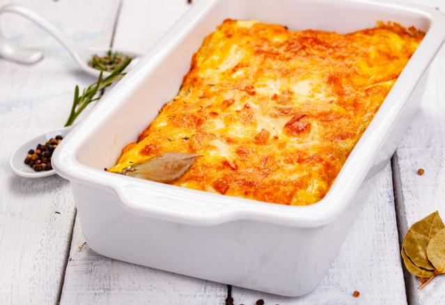 Baked curried fish loaf with a golden cheese topping in a white baking dish on a white table.