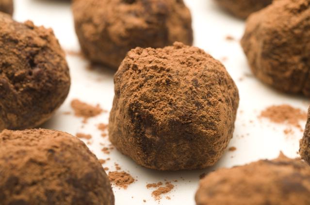 Close-up of round chocolate truffles coated in cocoa powder on a white plate, with cocoa dust scattered around them.