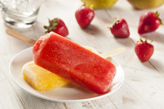 Red and yellow frozen yoghurt ice blocks on a white plate, with fresh strawberries scattered on the table nearby.