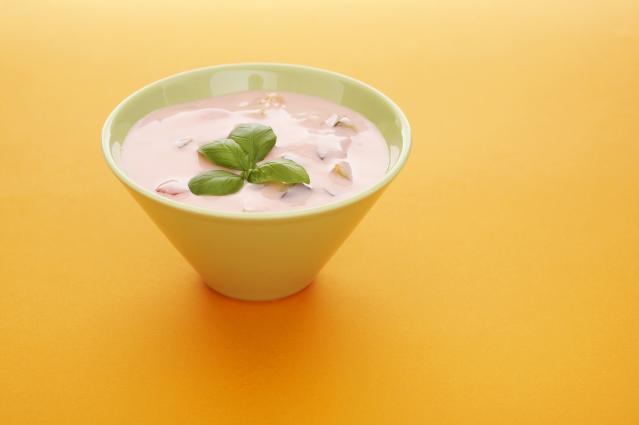 A small bowl of pink fruit yoghurt dessert topped with fresh basil leaves sits on a bright yellow background.