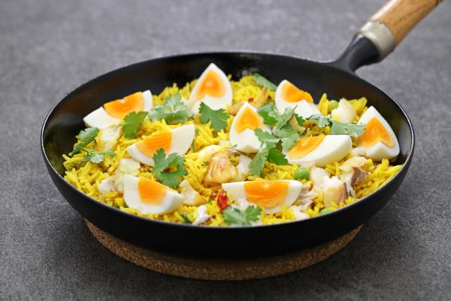 A frying pan filled with kedgeree made with yellow rice, fish, boiled eggs and fresh coriander.
