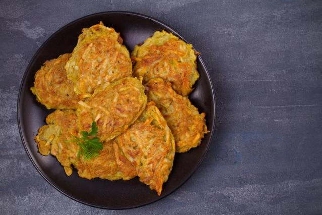 Plate of golden kūtai mussel and kūmara fritters garnished with herbs on a dark background.