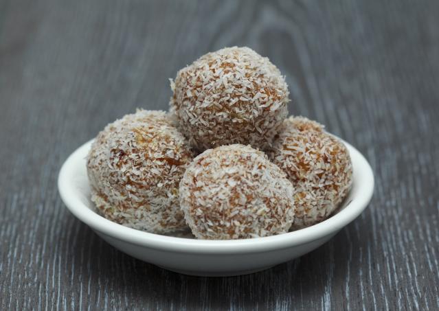 A small white bowl filled with coconut-coated kumara bliss balls on a dark wooden surface.
