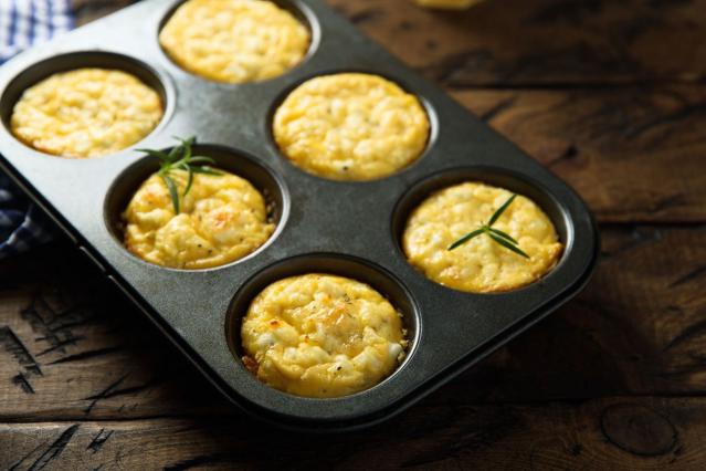 A muffin tray filled with baked mini kumara frittatas on a wooden table.