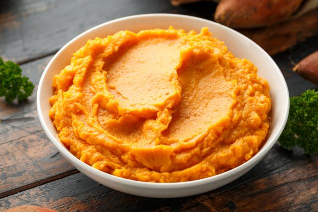 A bowl of smooth mashed orange kumara hummus on a wooden table.