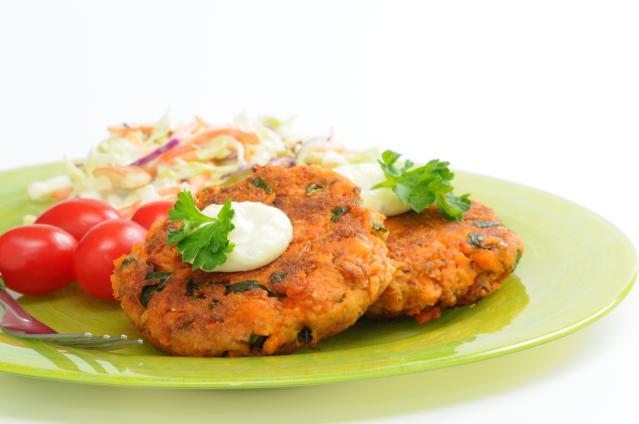 Lamb and kūmara patties on a green plate with coleslaw, cherry tomatoes and a dollop of sauce.
