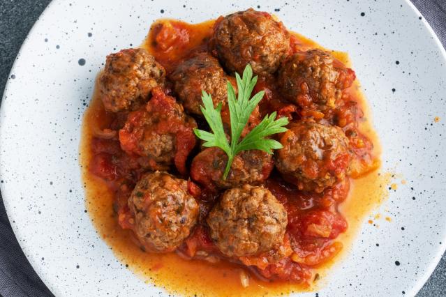 Meatballs in tomato sauce on a white plate, topped with a sprig of parsley.