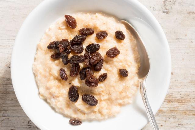 A bowl of creamy porridge topped with raisins and served with a spoon.