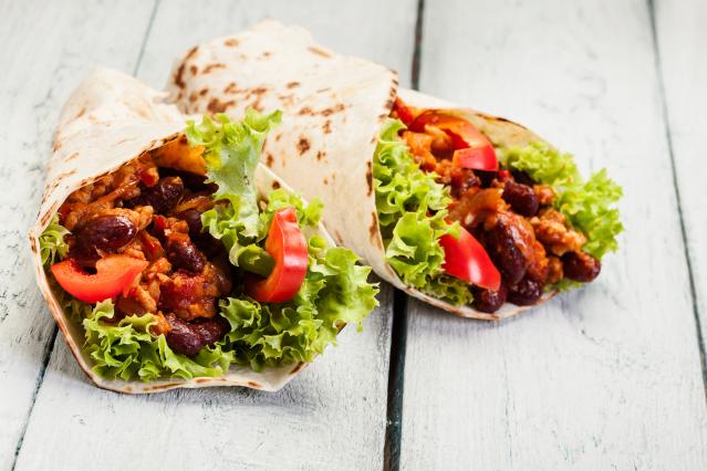 Two tortilla wraps filled with kidney beans, lettuce, tomato and a savoury mince mixture on a white wooden table.