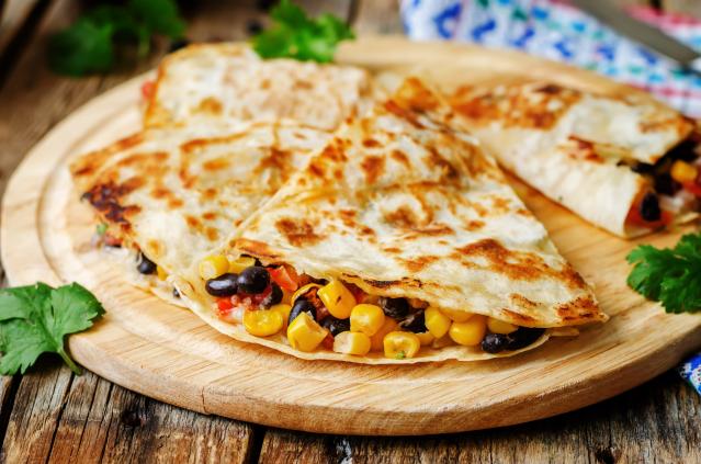 Toasted quesadillas filled with corn, beans and vegetables on a wooden serving board.