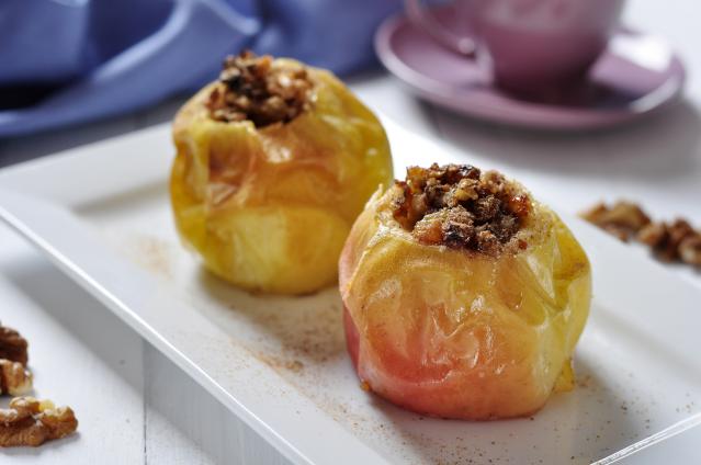 Two baked apples filled with a cinnamon and nut mixture on a white plate.