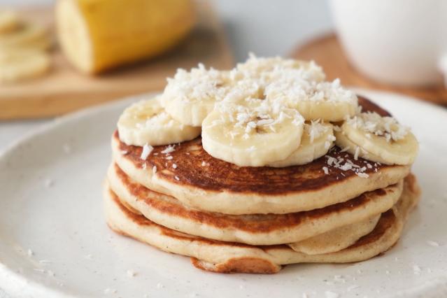 A stack of mini pancakes topped with sliced banana and shredded coconut on a white plate.