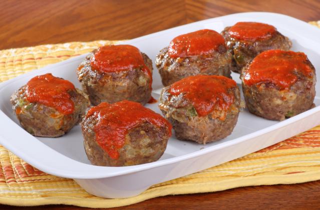 Mini meat loaves topped with tomato sauce in a white baking dish.