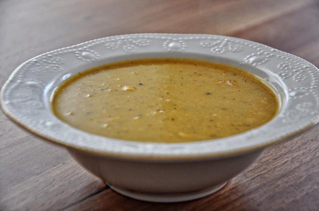A bowl of creamy pumpkin soup with herbs and small pieces of pumpkin, sitting on a wooden table.